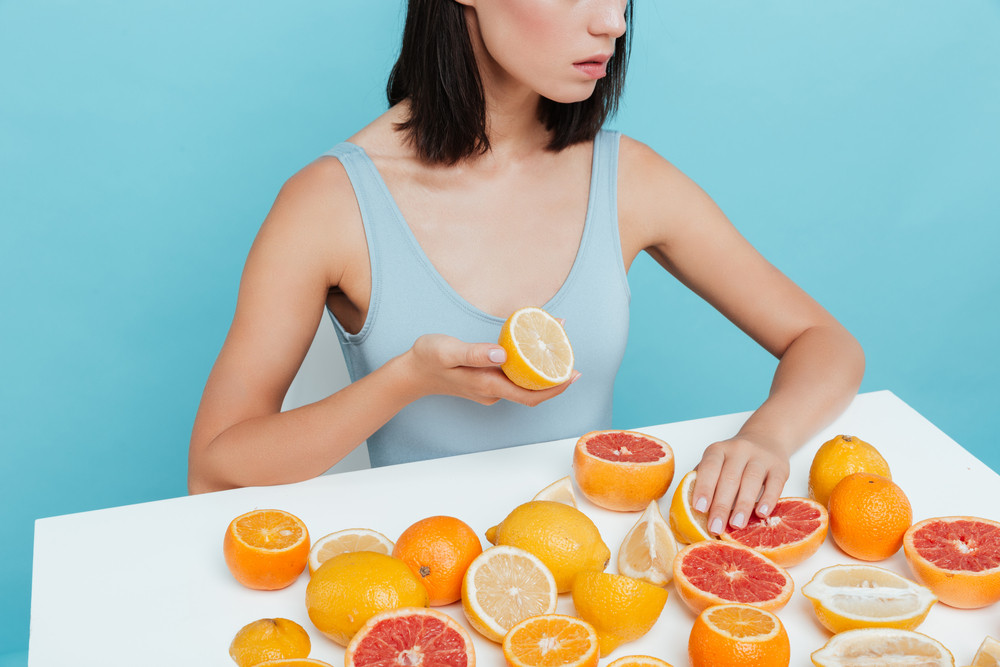 A woman sitting at table with many halves of oranges cut and spread out in front of her.